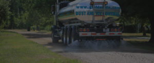 back photo of a truck spreading calcium chloride on an unpaved road