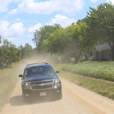 Photo of a dirty SUV driving down an unpaved road in the summer
