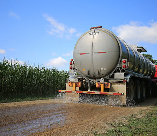 large truck spreading calcium chloride on a dirt road