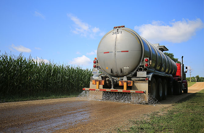 large truck spreading calcium chloride on a dirt road