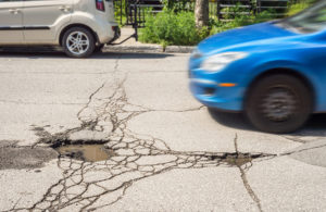 Photo of a blue car speeding toward a deep pothole