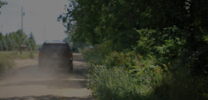 Photo of a dirt road in the summer with a car kicking up dust