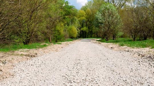 Contact Great Lakes Chloride to implement calcium chloride for Michigan Road Base Stabilization image shows gravel road next to trees